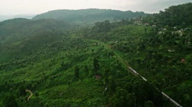 Demiryolunu çevreleyen Sri Lanka çay bahçeleri, seyahat manzarası. Drone sisli Haputale dağlarını aşan treni yakalıyor. Bulutlar yeşil tepelerin üzerinde süzülüyor, Asya 'da manzaralı bir yolculuk.