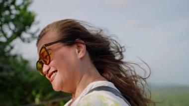 Canlı yapraklar titreşiyor, arka planda yeşil çimen dalgaları, gençliği taşıyor, altın saat ışığında özgürlük. Yaşlı Asyalı kadın gün batımında rüzgarı saçlarında hisseder, gözleri kapalı sevinçle gülümser. Yavaş çekim.