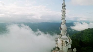 Sis yapıyı sarar, ağaçlar aşağıdan görülebilir. Sri Lanka tepelerindeki bulutların üzerinde yükselen Ambuluwawa Kulesi 'nin insansız hava aracı görüntüleri. Serene, hava perspektifi tropikal Asya 'daki sabah manzarasını yakalar.