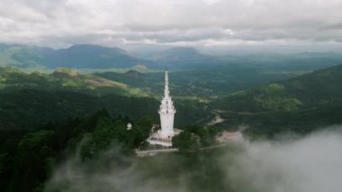 Hava görüntüsü, ağaç tepelerinin tepesinde dağ zeminine doğru ikonik bir yapının yükseldiğini gösteriyor. Sri Lanka 'daki Ambuluwawa Kulesi' nin insansız hava aracı. Ormanla çevrili, sis. Seyahat, kültür ve doğa temaları için mükemmel..