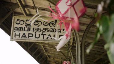 Tren yolcuları miras demiryolu platformunda yerel kültüre bakıyorlar. Sri Lanka 'daki Haputale istasyonuna yakın çekim, pembe dua bayraklarıyla dalgalanıyor. Asya 'da otantik seyahat anı. Yavaş çekim.
