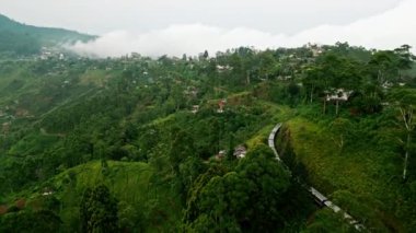 Yeşil tepelerin etrafında bulutlar uçuşuyor, Sri Lanka 'nın dağlık manzarası, Seylan' da manzaralı tren yolculuğu. Trenin Haputale 'den geçişini gösteren hava aracı görüntüleri, aşağıdaki zengin çay tarlaları..