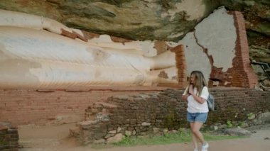 Namaste yapıyor, dini taş heykellere hayran. Sırt çantalı kıdemli Asyalı kadın dağlarda Buda mağarası keşfediyor. Yürüyüşçü dingin kültürel yürüyüşlerden, farkındalıktan ve sağlıktan hoşlanır..