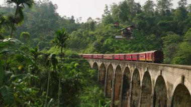 Muhteşem demiryolu yolculuğu, Asya 'da turistik manzaralı popüler turistik cazibe, tarihi mühendislik. Kırmızı tren, yeşil bitkilerle çevrili Ella, Sri Lanka 'daki ikonik dokuz kemer köprüsünden geçiyor..