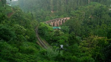 Ormanlarla çevrili tarihi demiryolu tepe kasabalarını, ikonik gezginleri, fotoğrafçıları birbirine bağlar. Güneş doğarken Sri Lanka 'daki Nine Arch Köprüsü' nün insansız hava aracı. Boş tren rayları, sakin doğanın ortasında macerayı bekliyor..