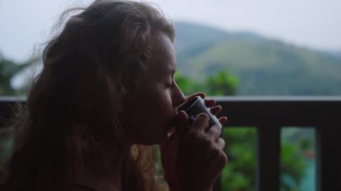 Siyah çayın tadını çıkarmak, huzurlu anın tadını çıkarmak, saçlarda hafif bir esinti, doğa güzelliği. Salıncakta çay yudumlayan bir kadın, sakin bir dağ zeminiyle, gölgeli terasta, zengin çay tarlasına bakan bir kadın. Yavaşla