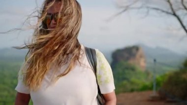 Deneyimli yürüyüşçü, Sri Lanka manzarasının bitkilerinin arasında manzaralı patikaları keşfeder, macerayı somutlaştırır, canlılık katar. Enerjik kıdemli Asyalı kadın kayalık arazide yürüyüş yapıyor, arka planda Sigirya Kayası yükseliyor.