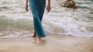 Yavaş çekimde zarif adımlar, dalgalar ayakların üzerinden yavaşça geçer. Mavi elbiseli çıplak ayaklı kadın kumlu sahilde denizden çıkar. Bileklik güneş ışığında parıldıyor. Gezinti gibi. Romantik, huzurlu bir tatil..