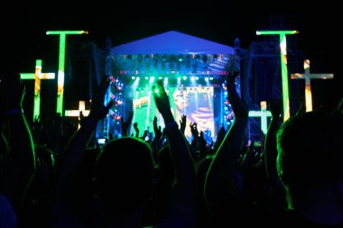 İnananlar toplanın, ruhani konserin tadını çıkarın, inancı ve birliği ifade edin. Enerjik kalabalık gece müzik festivalinde el kaldırıyor, sahneyi bando ile aydınlatıyor, ışıklar şenlikli atmosfer yaratıyor.