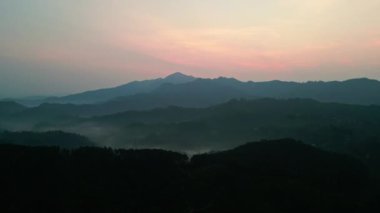 Pembe ve turuncu tonlarda gökyüzünü boyarken, zirveler arasında sis süzülür. Sri Lanka 'daki Ella dağları üzerinde insansız hava aracı gün doğumu. Sessiz, sakin manzara uyanıyor, gün doğayla iç içe başlıyor..