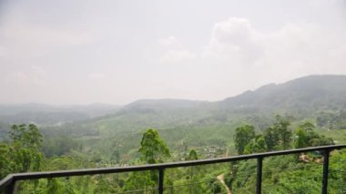 Güneşli gökyüzünün altındaki yeşil tarlalar. Sri Lanka 'daki zengin Haputale çay çiftliklerinin panoramik manzarası. Tropikal manzaradaki tepeler ve yerel köy. Tarım turizmi, dingin doğa, ekolojik seyahat.
