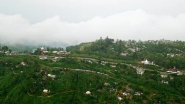 Bulutlar yeşil yamaçların üzerinde süzülüyor, Sri Lanka 'da hareket halindeki tren, sakin ve manzaralı bir seyahat noktası ile kırsal bir manzara gözler önüne seriliyor. İnsansız hava aracı treni Haputale Dağı çay tarlalarından geçiyor..