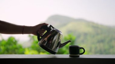 Manzaralı çay bahçesine karşı kupanın üzerinden buhar yükseliyor. Kadın terasta, dağ sırasına bakan bardağa taze çay dolduruyor. Gün doğumunda doğal ortamda aromatik içecek hazırlığı. Yavaş çekim.