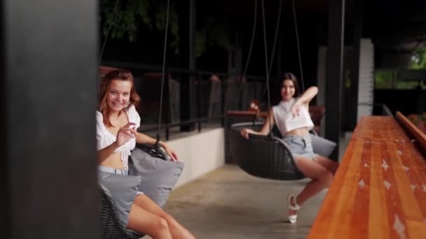 Hübsche Freundinnen Reiten Auf Einer Gemütlichen Schaukel Mit Kissen Und — Stockvideo