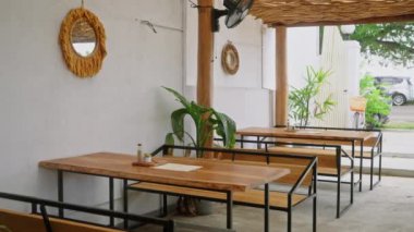 Kafe terasında ahşap masalar, banklar, yeşil saksı bitkileri. Boş tropikal açık hava restoranı, saman çatı, duvarında dekor. Kafe terasında kimse yok. Dinlen, rahat bir yerde rahatla..