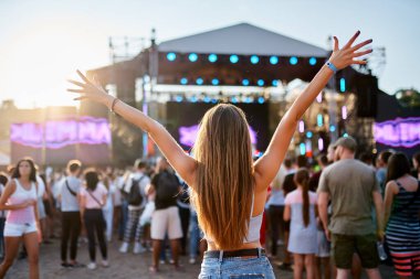 Arkadaşlar toplanır, günbatımında canlı müziğin tadını çıkarırlar. Yaz plaj festivalindeki uzun saçlı kızın arka görünüşü, sahnenin yakınında sevinçten kollarını kaldırıyor. Gençler coşkulu bir atmosferle kutlama yapıyor, kıyı etkinliğinde dans ediyor..