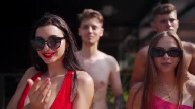 Yaz havuzu partisinde renkli bikiniler ve güneş gözlükleriyle poz veren, dans eden ve flört eden kadın ve erkekler. Arkadaşlar tatil için havuz ve dinlenme yerlerinde tatil yapıyorlar..