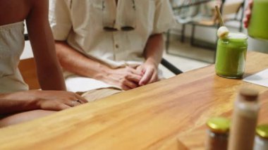 Garson, Bali 'deki kafede aşık çiftler için meyve suyu ve pipetle ahşap masaya koyuyor. Garsonun eli müşterilere sağlıklı içkiler dağıtıyor. Kadın ve erkek içecek alıyor. Yakın plan..