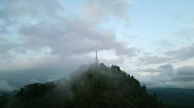 Şafak sökerken yemyeşil manzara etrafını sarar. Kutsal mekan panoramik manzaralardan ve barıştan ilham alır. İnsansız hava aracı, Sri Lanka dağının sisli tepesinde, ruhani birliğin sembolü olan Ambuluwawa Kulesi 'nin etrafında döner..