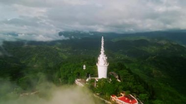 Kutsal mimari ayakta duruyor, barış, birlik, çeşitli dinler. İnsansız hava aracı Ambuluwawa Kulesi 'ni, Sri Lanka' yı sisli yeşil dağları sisle kaplıyor. Ziyaretçiler tırmanıyor, çok inançlı anıtı keşfediyor, görüşler.