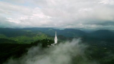 Şehir simgesi çevresindeki panoramik manzara yeşil orman arazisini ortaya çıkarıyor. Sri Lanka 'daki Ambuluwawa Kulesi' nin sisli dağların üzerinden yükselen insansız hava aracı görüntüleri. Kültürel mimariyle ruhsal ya da seyahat teması. Havadan