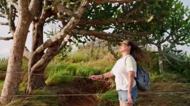 Saçlar rüzgarda özgürce dalgalanır. Güneş gözlüklü Asyalı son sınıf öğrencisi gün batımında yeşillikte neşe hisseder. Sıradan giyinerek, gençliği somutlaştırıyor. Özgürlük, doğanın güzelliğini aldıkça parlıyor. Yavaş çekim.