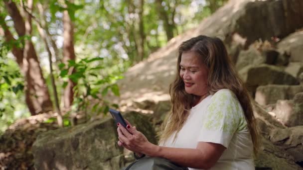 她独自在树上 石头上寻找快乐的捕捉时刻 亚洲老年妇女笑着 在登山假期间用智能手机进行自我锻炼 老徒步旅行者喜欢科技 记忆和户外旅行 — 图库视频影像