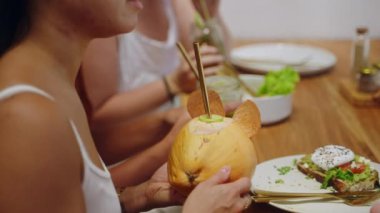 Kadın ellerinde hindistan cevizi kokteyli. Genç bir kadın tropikal kafede arkadaşlarıyla konuşuyor. Lezzetli yemekler ve sağlıklı içecekler masada. Sri Lanka 'da arkadaşlarıyla restoranda oturan hoş bir kız. Yakın plan..