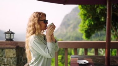 Rahat bir sabah, nefes kesici manzaralı lüks bir tatil köyünde. Zarif bir kadın dağlara bakan manzaralı terasta kahveyi sever. Leydi doğada lüks seyahat anlarının tadını çıkarıyor. Yavaş çekim.