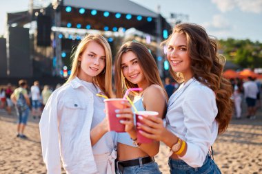 Paylaştığımız sevinç anları, festivalin arka planına bardakları tokuşturmalar, yaz eğlencelerinin somutlaşması. Gün batımında bir plaj müzik festivalinde renkli içeceklerle kadeh kaldıran bir grup genç kız..