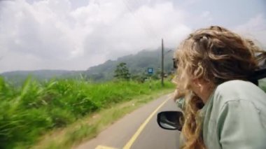 Gülümser, neşe hisseder, temiz havada elini uzatarak özgürlüğünü hisseder, güneş ışığında doğanın güzelliğini keşfeder. Sarışın kadın araba camından sarkmış, rüzgar gibi esen saçlar manzaralı dağ yolculuğunda. Yavaşla