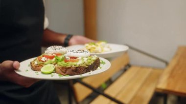 Garson elleri vejetaryen yemeği taşır, avokado tostları da kafede mutlu genç kadınlar için. Garson müşterilere sağlıklı yemek veriyor. Çeşitli bayan arkadaşlar restoranda lezzetli yemekler yerler. Yakın plan..