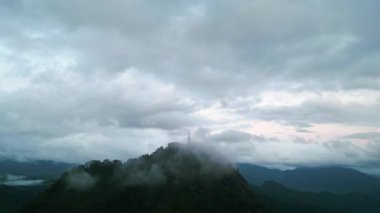 Sis bulutu dağları, şafak vakti manzarayı sarıyor. Sri Lanka 'daki yemyeşil ormanlarla çevrili Ambuluwawa Kulesi üzerinde insansız hava aracı uçuşu. Seyahat, doğa, macera arayanlar büyüleyici bir sahne..