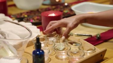 Spa ve sağlık merkezinde rahatlamak için mum yakıyorum. Mumlarla, kurutulmuş çiçeklerle ve beyaz havlularla güzel bir kompozisyon. Kadın eli uzanıyor ve masadan kremalı bir cam kase alıyor.