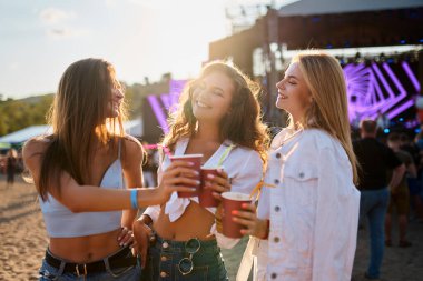 Gülümseyen arkadaşlar yaz festivali havasının tadını çıkarırlar. Sahildeki müzik etkinliğinde bir grup kadın bardaklarla kadeh kaldırıyor. Dans ederek parti atmosferi, denizle kahkaha. Günlük kıyafetler, gün batımı ışığı, neşeli kutlamalar..