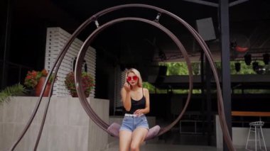 Çekici gülümseyen kız poz veriyor, oturuyor ve salıncak sürüyor. Lüks tatil köyü sahil kulübünün tezgahında mayo giyip el sallıyor ve hava öpücüğü yolluyor. Arkadaşlarla tatilde havuz partisi.