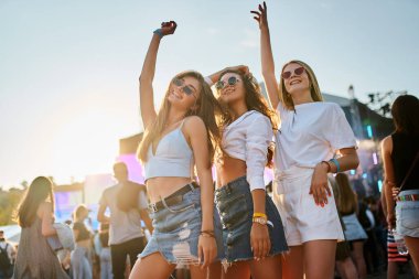 Kadınlar dans eder, güneş ışığında gülümserler. Bir grup farklı kız kıyı müzik festivalinde eğleniyor. Arkadaşlar canlı müzik grubunu, kumsalda gün batımı partilerini severler. Gençlik kültürü, yaz etkinliği.