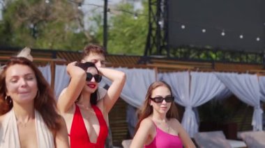 Bir grup renkli bikinili arkadaş yaz partisinde lüks kulüp terasında yüzme havuzunda yürüyorlar. Mayolu kadın ve erkek plaj tatil köyünde dinlenecekler..