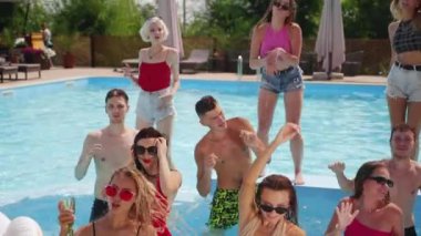 Kadın ve erkek modeller yüzme havuzunda takılıyor, su sıçratıyor, flört ediyor ve poz veriyorlar. Mayolu ve güneş gözlüklü bir grup arkadaş yaz tatillerinde eğlenir ve dinlenir..