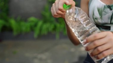 Antrenman kıyafeti, akıllı seğirme, susuzluğu giderme, susuzluğun önemi. Bitkin düşmüş sporcu kadın yeşilliklerle çevrili açık hava fitness merkezinde eğitimden sonra temiz suyla sulanıyor. Yavaşla