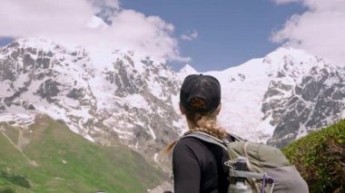 Yürüyüşçü kadın, Büyük Kafkasya Dağları 'ndaki Svaneti dağlarının manzarasını seviyor. Karlı tepelere bakıyor, sırt çantası takıyor, açık hava kıyafetleri giyiyor. Çarpıcı doğa ortamında yakalanmış. Macera, yürüyüş seyahati.