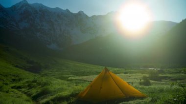 Svaneti Janga tepesindeki dağlı çadır zamanı. Güneş doğar, ışık yeşil araziye yayılır. Açık hava kampı, Kafkasya dağlarında manzara manzarası. Macera gezisi. Zaman Uygulaması