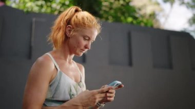 Çalışma sürecini, sağlık verilerini izliyor. Kızıl saçlı bayan sporcu spor salonundaki akıllı telefondan fitness uygulamasını kontrol ediyor. Teknolojiden anlayan sporcu kadın fitness rejimini ve gol atmayı sürdürüyor. Yavaşla