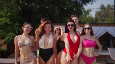 Bir grup renkli bikinili arkadaş yaz partisinde lüks kulüp terasında yüzme havuzunda yürüyorlar. Mayolu kadın ve erkek plaj tatil köyünde dinlenecekler..