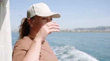 Deniz yolculuğunda olan bir kadın yolcu. Kadın gülümsüyor, feribottan okyanus manzarasını seviyor. Turist, şehrin ufuk çizgisini, deniz kenarını gözlemliyor. Güneşli bir gün, tatil seyahati, feribot yolculuğu tecrübesi. Rahatla, turistik yerler, turizm.