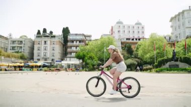 Turistler boş gezintilerden, manzaralı şehir manzaralarından hoşlanırlar. Büyükada adası meydanında pembe bisikletli bir kadın. Bisiklet macerasında tek başına seyahat eden şehir kültürü yaşıyor..