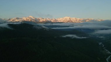 Gün doğumunda Mestia 'daki Svaneti dağlarının hava manzarası. Karla kaplı tepeler, sisli yeşil vadiler, aşağıdaki nehir. Bulut katmanları, dağ sıraları huzur dolu manzaralar. Sabah ışığı araziyi aydınlatır. İHA