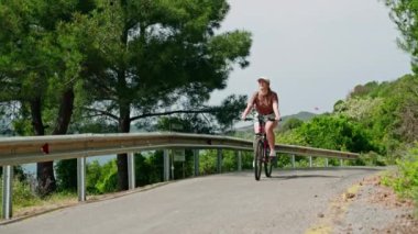 Ağaçlar ve okyanus manzarası. Büyükada Adası manzaralı bir yolda bisiklet süren bir kadın. Bisikletçi doğayı, boş zamanı seviyor. Açık hava fitness, seyahat yaşam tarzı.