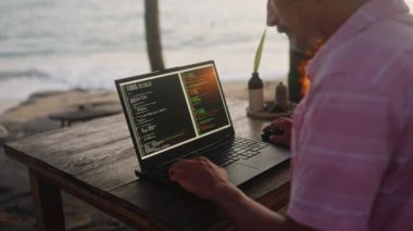 Okyanus dalgaları, sıcak ışık, erkek programcının denize yakın yazılımları kodlaması gibi sakin bir zemin. Web geliştiricisi günbatımında deniz kenarındaki kafede dizüstü bilgisayarda çalışır, ekranda kodlu programlama yapar. Yavaş çekim.