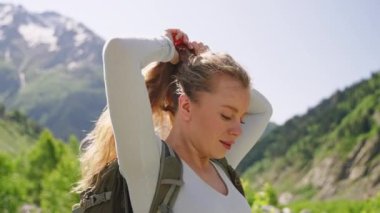 Dağlarda yürüyüş yapan genç bir kadın, at kuyruğu, güneş ışığı, temiz hava, yeşil manzara yapmak için duruyor. Sırt çantası, doğa macerası, açık hava aktivitesi. Yaz sağlıklı yaşam tarzı. Vahşi doğayı seven bir kadın..